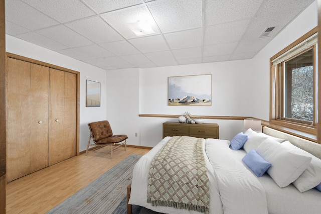 bedroom with wood-type flooring, a paneled ceiling, and a closet