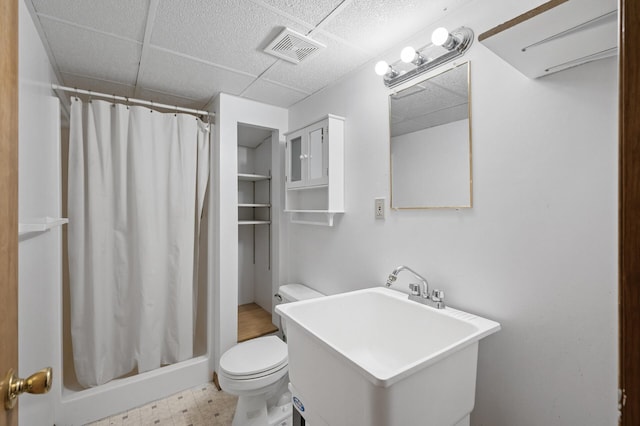 bathroom featuring a drop ceiling, sink, toilet, and walk in shower