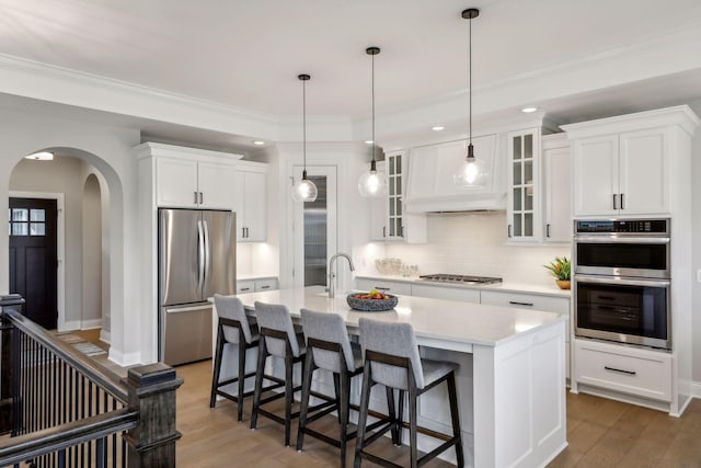 kitchen with an island with sink, stainless steel appliances, white cabinets, hardwood / wood-style flooring, and a kitchen breakfast bar