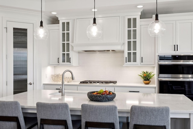 kitchen featuring an island with sink, hanging light fixtures, white cabinetry, stainless steel appliances, and a breakfast bar