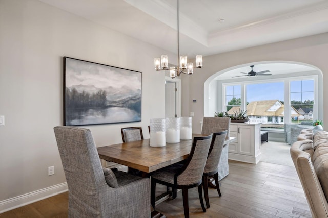 dining space featuring ceiling fan with notable chandelier, ornamental molding, light wood-type flooring, and a raised ceiling