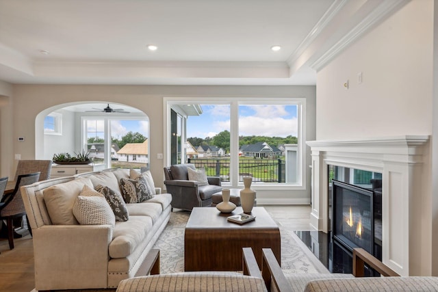 living room with light wood-type flooring, ceiling fan, crown molding, a tray ceiling, and a premium fireplace