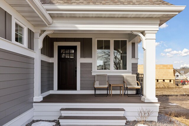 view of exterior entry featuring covered porch and a shingled roof