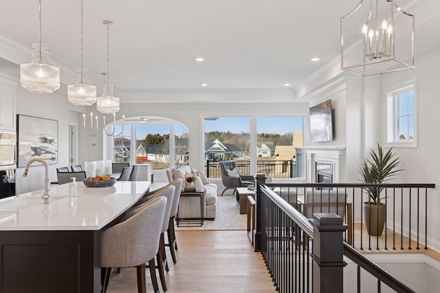 kitchen featuring ornamental molding, pendant lighting, light wood-type flooring, and a kitchen island with sink