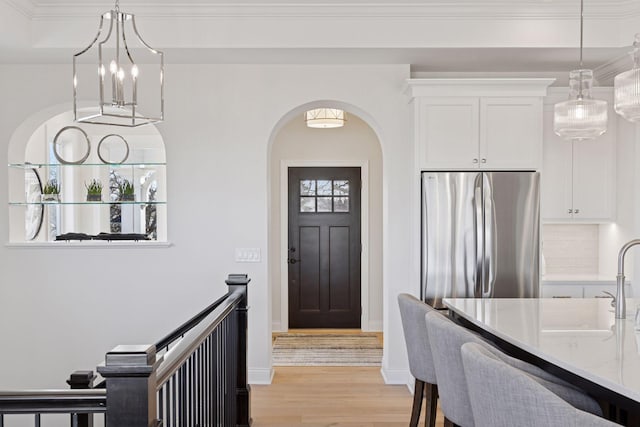 entrance foyer featuring arched walkways, baseboards, light wood finished floors, and ornamental molding