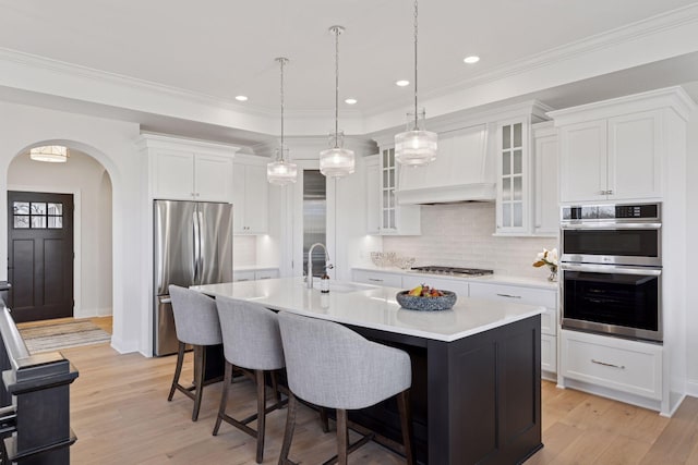 kitchen featuring a breakfast bar area, light countertops, custom range hood, appliances with stainless steel finishes, and arched walkways