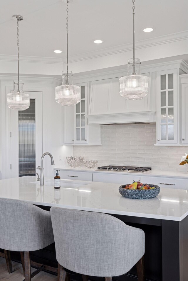 kitchen featuring ornamental molding, custom range hood, decorative light fixtures, light countertops, and stainless steel gas cooktop