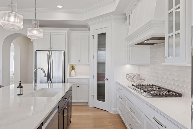 kitchen with a sink, white cabinetry, stainless steel appliances, a raised ceiling, and custom exhaust hood