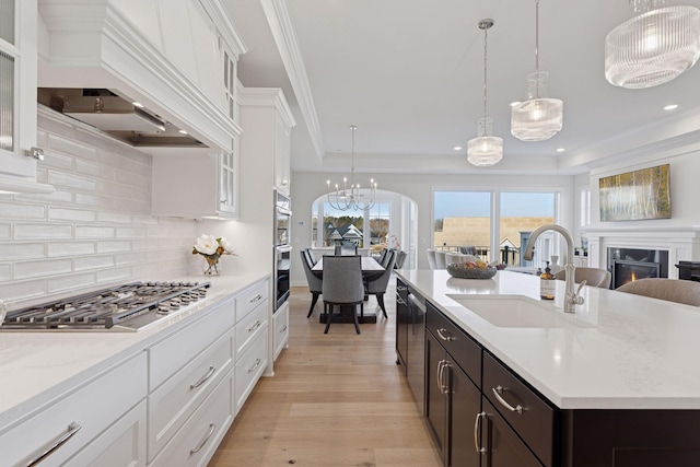 kitchen with premium range hood, light wood-type flooring, white cabinets, stainless steel appliances, and a sink