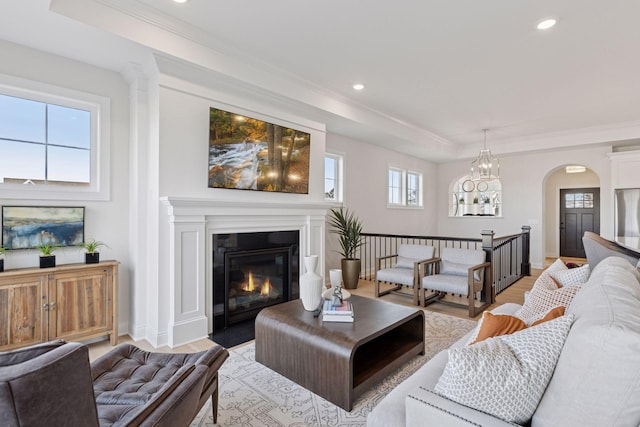 living area with crown molding, a fireplace with flush hearth, arched walkways, and light wood finished floors