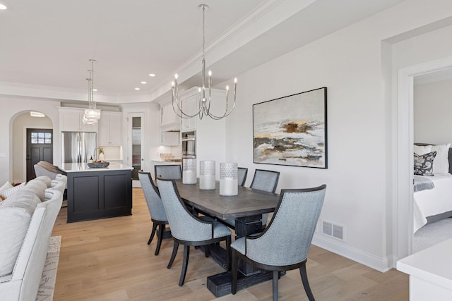 dining room with crown molding, light wood-style floors, arched walkways, and visible vents