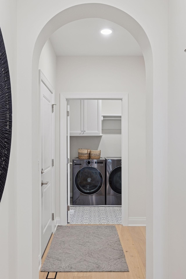 laundry room featuring wood finished floors, baseboards, laundry area, arched walkways, and independent washer and dryer