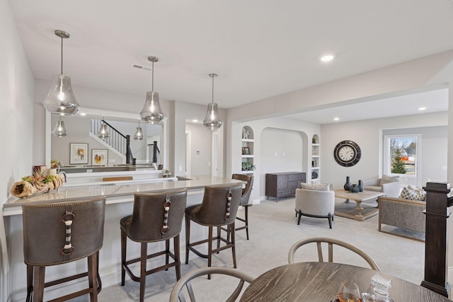 kitchen featuring visible vents, built in shelves, arched walkways, a breakfast bar area, and light colored carpet