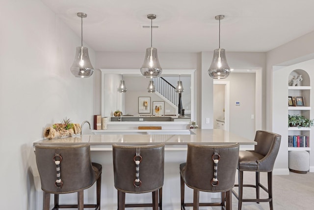 kitchen featuring hanging light fixtures, visible vents, a kitchen bar, and carpet floors