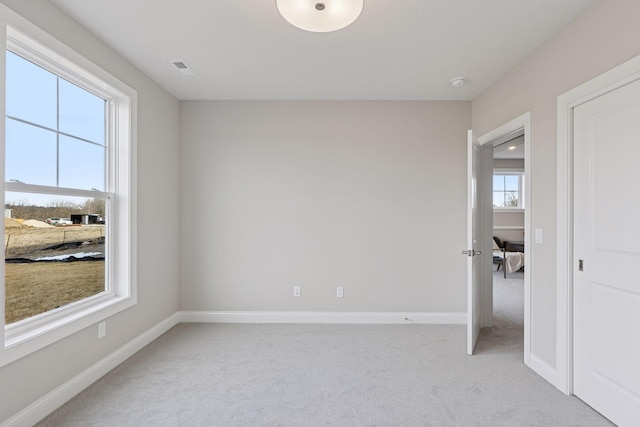 unfurnished room with visible vents, light colored carpet, and baseboards