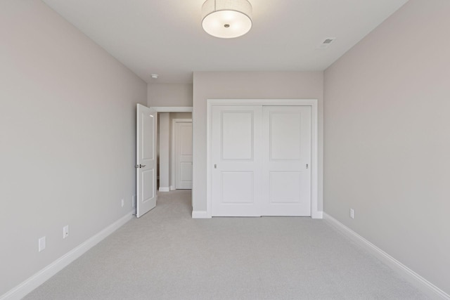 unfurnished bedroom with a closet, visible vents, light colored carpet, and baseboards