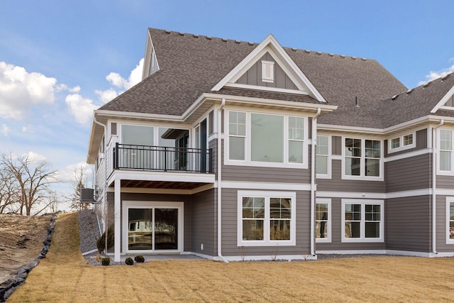 rear view of property featuring central air condition unit, a balcony, a lawn, and a shingled roof