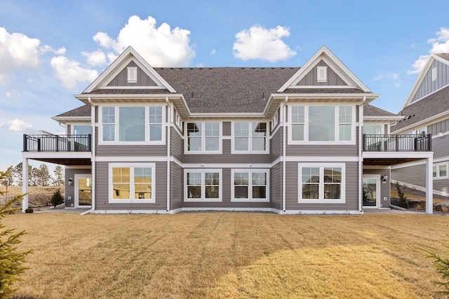 back of property with a balcony, a yard, and roof with shingles