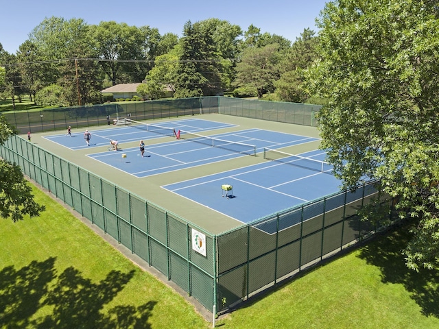 view of tennis court with a lawn and fence