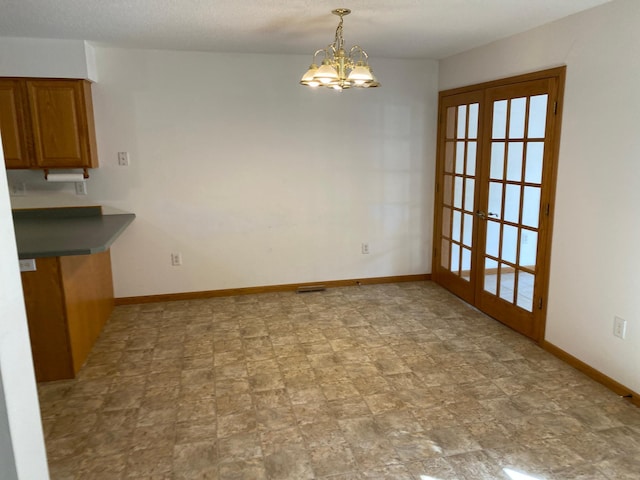 unfurnished dining area with french doors, an inviting chandelier, and a textured ceiling