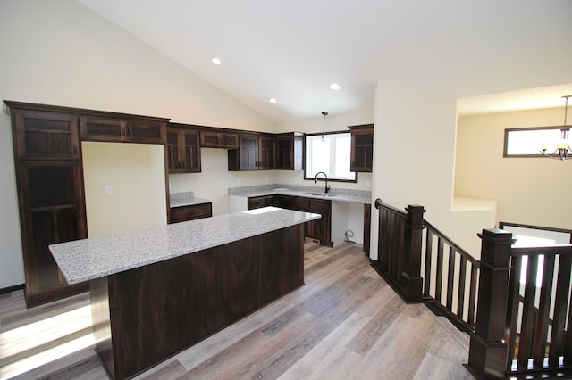 kitchen featuring light stone countertops, dark brown cabinetry, a center island, decorative light fixtures, and sink