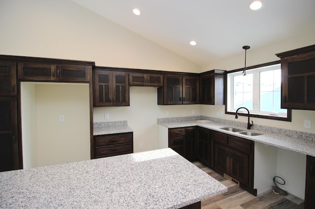 kitchen with vaulted ceiling, light stone countertops, hanging light fixtures, and sink