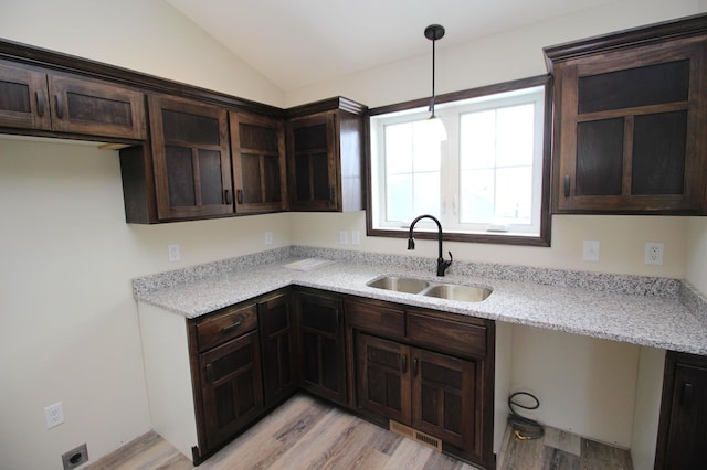 kitchen featuring light hardwood / wood-style floors, hanging light fixtures, light stone countertops, vaulted ceiling, and sink