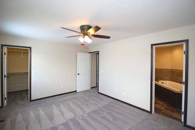 unfurnished bedroom with ensuite bath, a walk in closet, a closet, ceiling fan, and light colored carpet