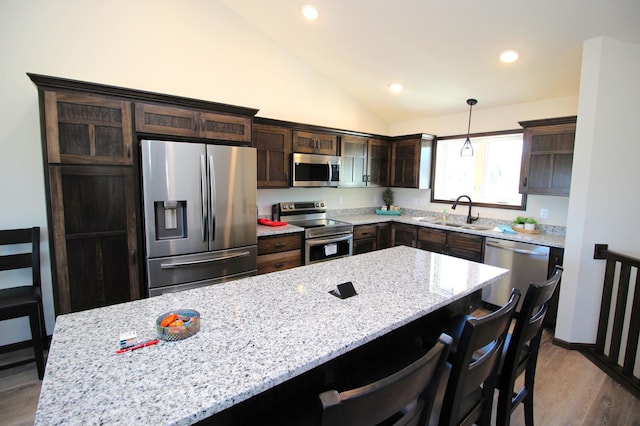 kitchen featuring a sink, stainless steel appliances, dark brown cabinetry, light stone countertops, and vaulted ceiling