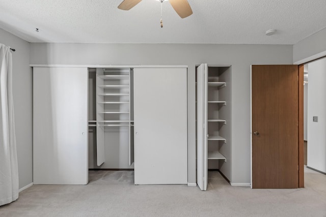 unfurnished bedroom with a textured ceiling, ceiling fan, multiple closets, and light colored carpet