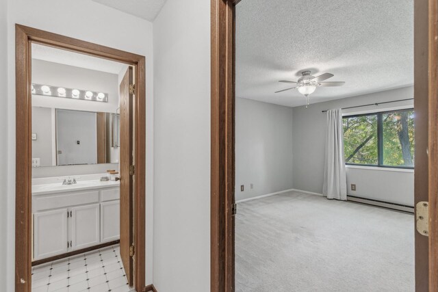 hallway with sink, a baseboard heating unit, a textured ceiling, and light carpet