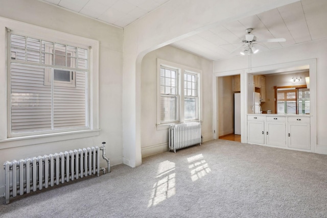 interior space featuring ceiling fan, light colored carpet, and radiator heating unit