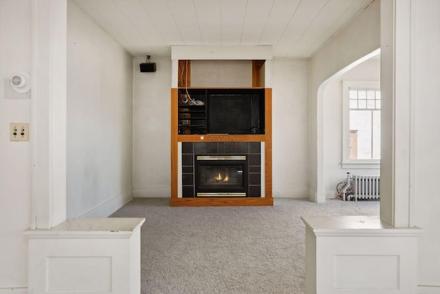 unfurnished living room with carpet floors, radiator, and a tile fireplace