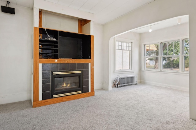 unfurnished living room featuring carpet floors, radiator heating unit, and a fireplace