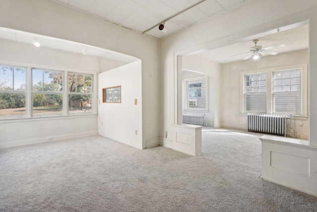 carpeted empty room with ceiling fan, radiator, and rail lighting