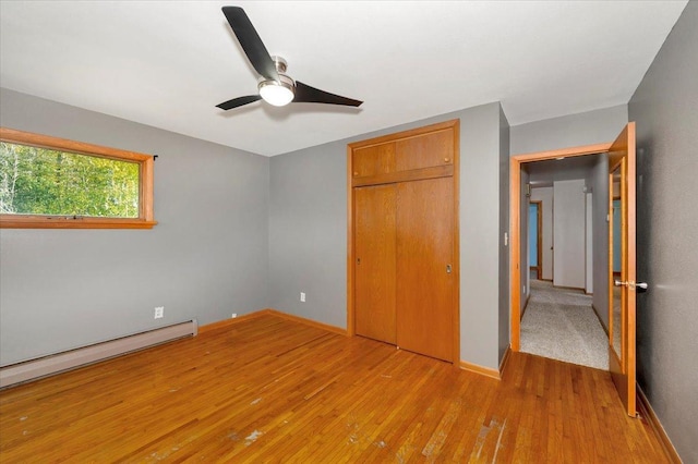 unfurnished bedroom with a baseboard radiator, light hardwood / wood-style floors, a closet, and ceiling fan