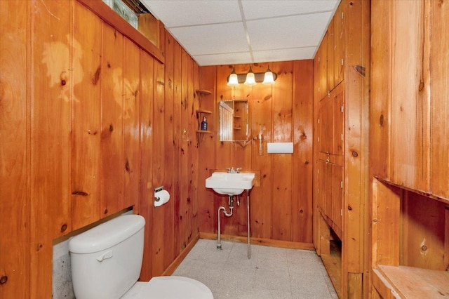 bathroom featuring a drop ceiling, sink, toilet, and wood walls