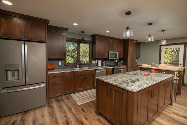 kitchen with light wood-type flooring, pendant lighting, tasteful backsplash, light stone counters, and appliances with stainless steel finishes