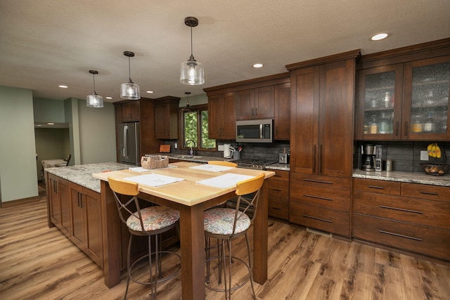 kitchen with light stone counters, decorative light fixtures, light hardwood / wood-style flooring, stainless steel appliances, and decorative backsplash