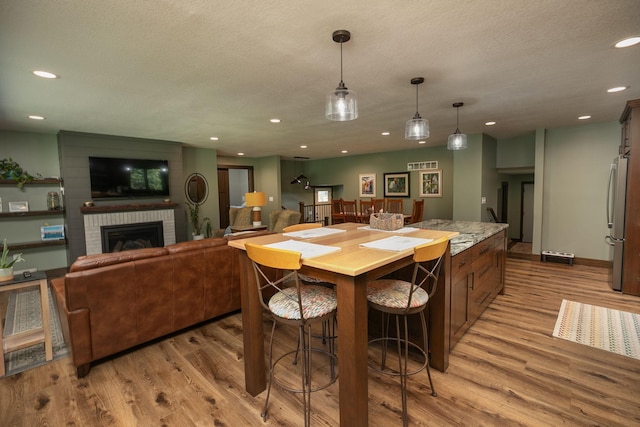 kitchen with a fireplace, pendant lighting, stainless steel refrigerator, and light hardwood / wood-style flooring