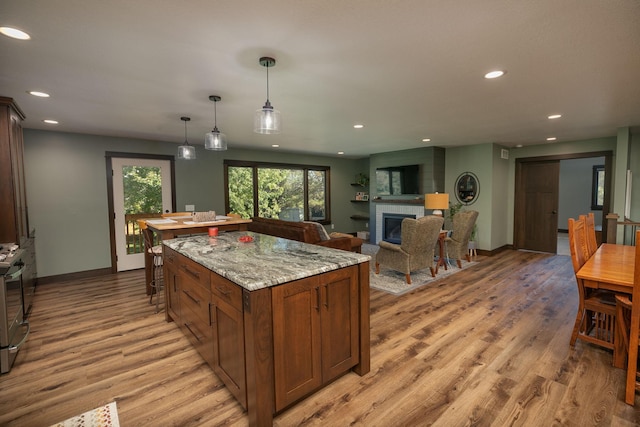 kitchen featuring light hardwood / wood-style floors, pendant lighting, a kitchen island, light stone counters, and stainless steel range oven