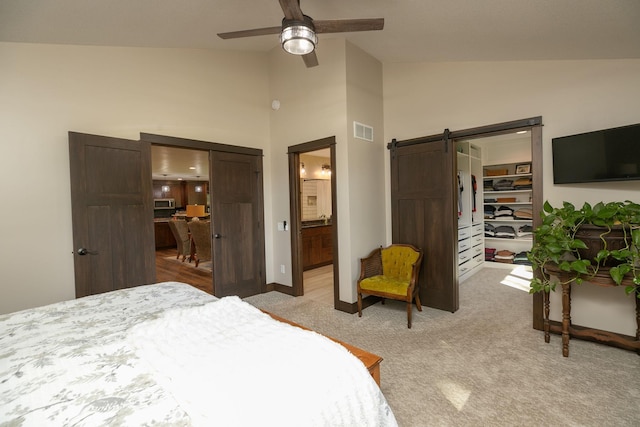 carpeted bedroom with ceiling fan, lofted ceiling, connected bathroom, and a barn door