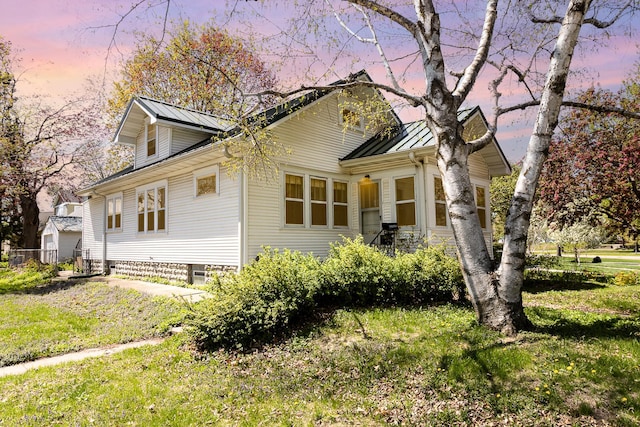 property exterior at dusk with a standing seam roof, metal roof, and a lawn