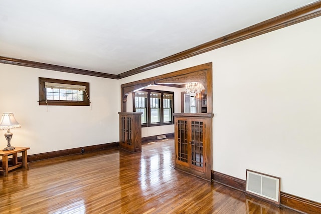 empty room with ornamental molding, baseboards, wood finished floors, and arched walkways