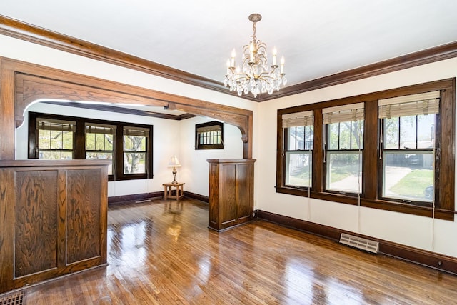 unfurnished dining area with arched walkways, a chandelier, baseboards, crown molding, and dark wood-type flooring