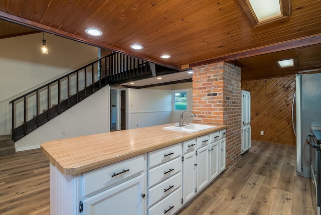 kitchen with white cabinetry, pendant lighting, wood-type flooring, wooden walls, and sink