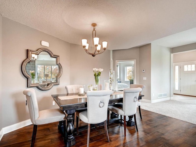 dining space with dark wood-type flooring, an inviting chandelier, and a textured ceiling