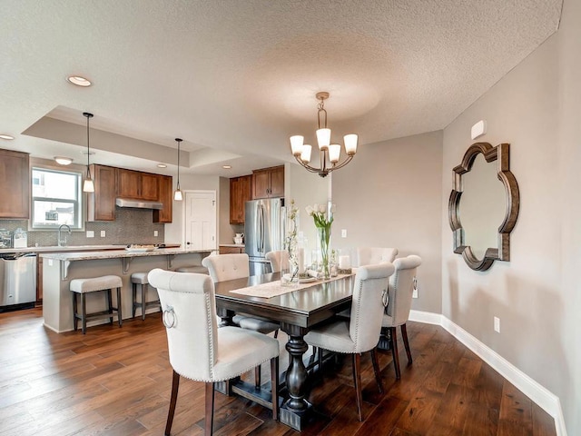 dining area with sink, a textured ceiling, a tray ceiling, a notable chandelier, and dark hardwood / wood-style flooring