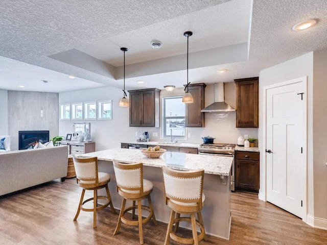 kitchen featuring hardwood / wood-style floors, a center island, wall chimney range hood, hanging light fixtures, and a kitchen breakfast bar