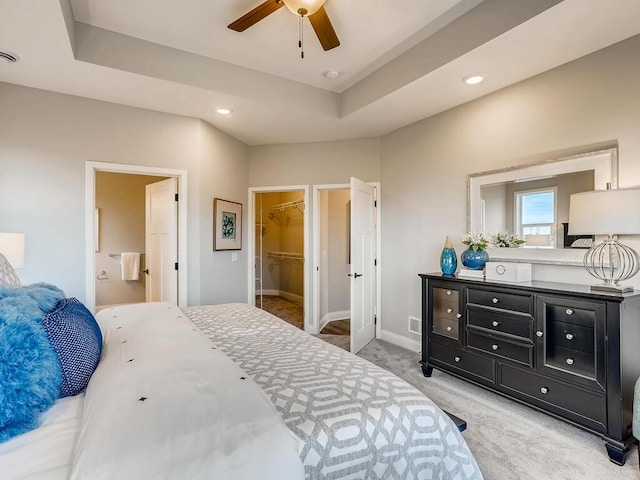 bedroom featuring a tray ceiling, a closet, light carpet, a spacious closet, and ceiling fan